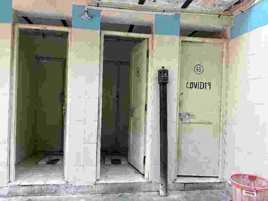 View of three poorly maintained community toilet cubicles, with 'COVID-19' painted on the door of one cubicle